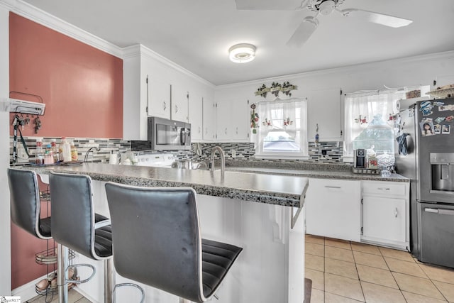 kitchen with stainless steel appliances, tasteful backsplash, kitchen peninsula, white cabinets, and ornamental molding