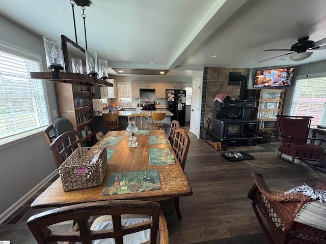 dining space with a wood stove, ceiling fan, dark hardwood / wood-style flooring, and a healthy amount of sunlight