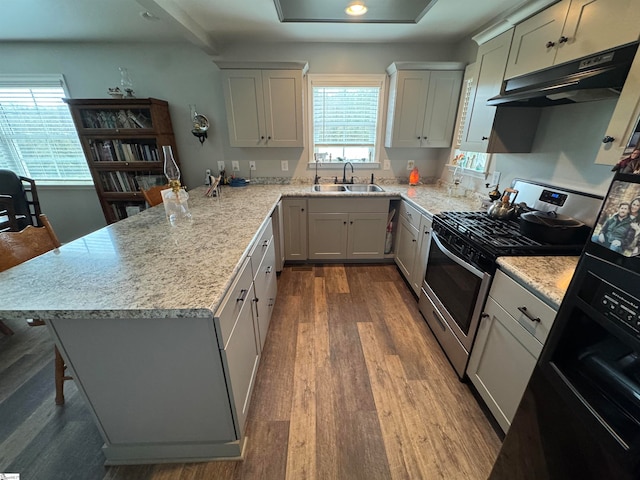 kitchen featuring hardwood / wood-style flooring, stainless steel gas range oven, white cabinets, and sink