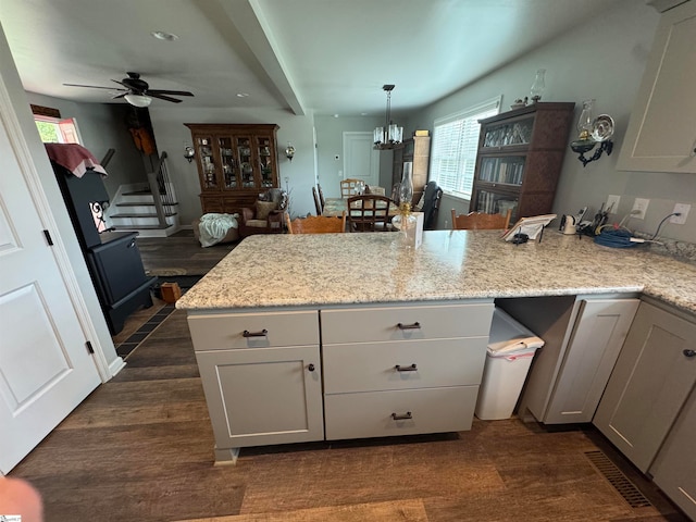 kitchen with ceiling fan with notable chandelier, light stone countertops, decorative light fixtures, dark hardwood / wood-style flooring, and kitchen peninsula