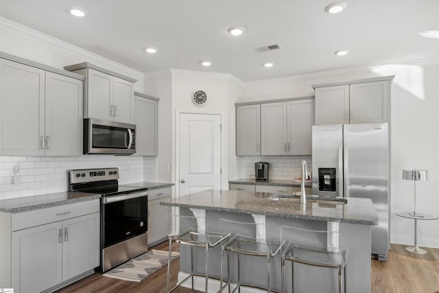 kitchen with stainless steel appliances, sink, light hardwood / wood-style flooring, gray cabinets, and an island with sink