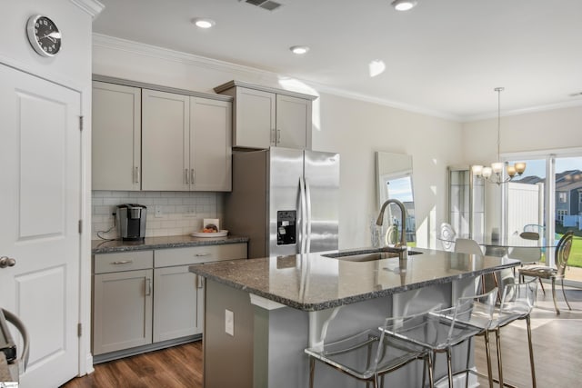 kitchen featuring gray cabinetry, sink, stainless steel fridge with ice dispenser, dark stone countertops, and an island with sink