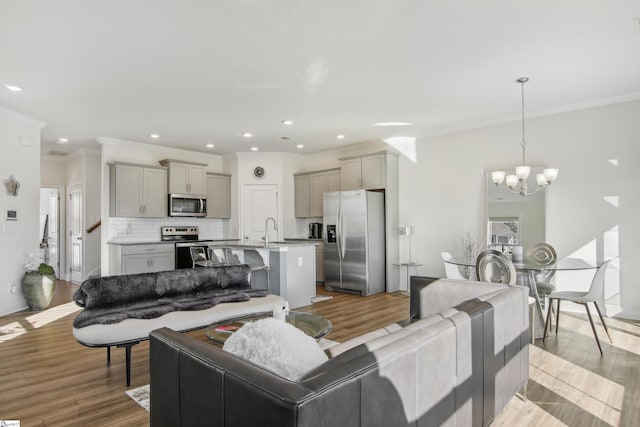 living room featuring sink, ornamental molding, a notable chandelier, and light wood-type flooring