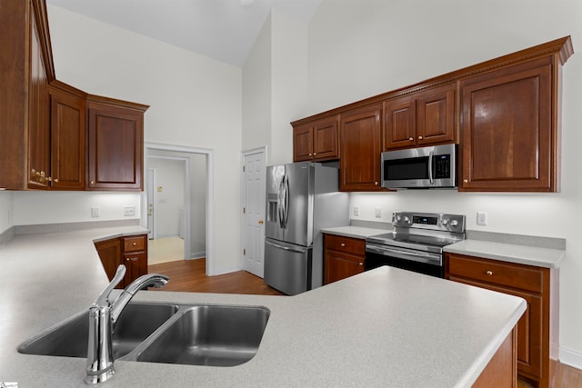 kitchen with kitchen peninsula, stainless steel appliances, high vaulted ceiling, and sink