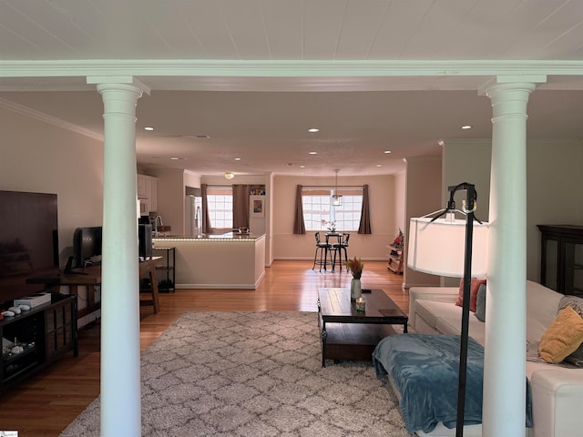 living room with light wood-type flooring, crown molding, and ornate columns