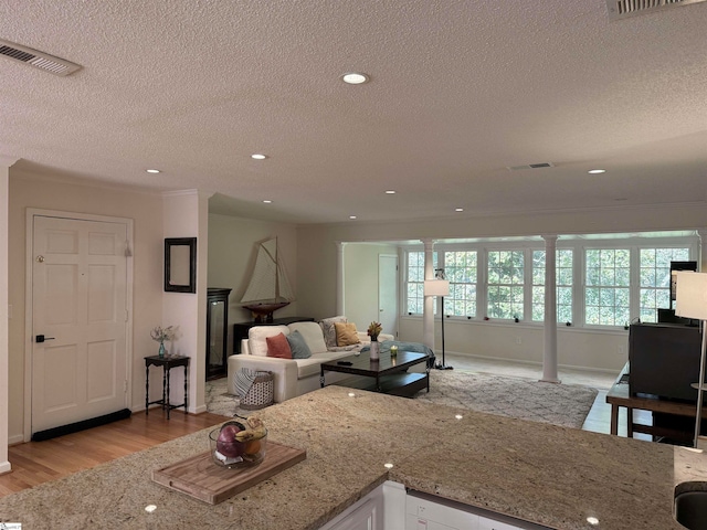 kitchen featuring white cabinets, light stone countertops, light wood-type flooring, a textured ceiling, and ornate columns