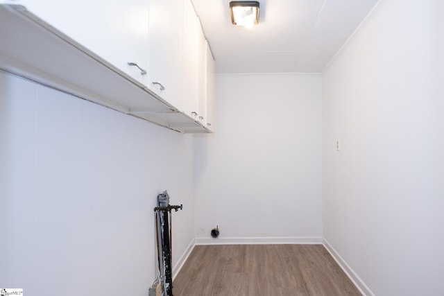 clothes washing area featuring ornamental molding, cabinets, and light wood-type flooring