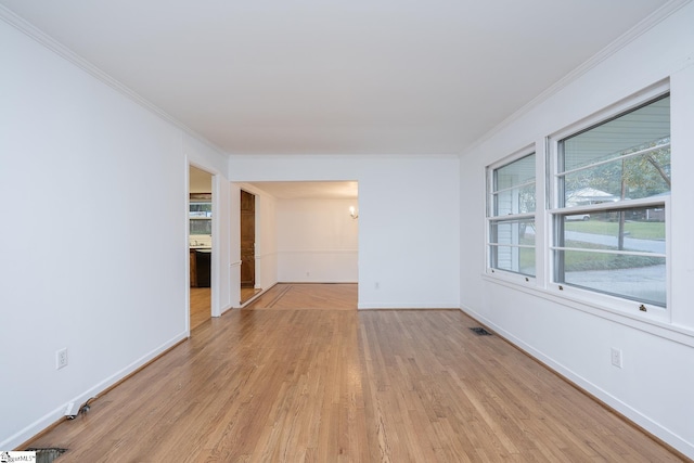 empty room featuring crown molding, a wealth of natural light, and light wood-type flooring