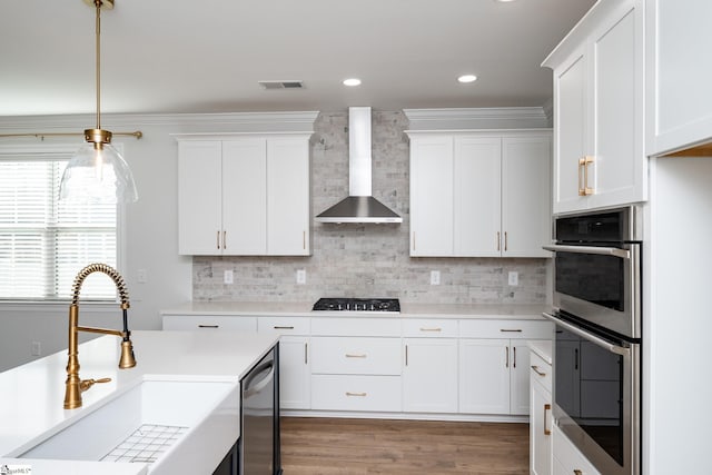 kitchen featuring appliances with stainless steel finishes, wall chimney exhaust hood, sink, hardwood / wood-style flooring, and white cabinetry