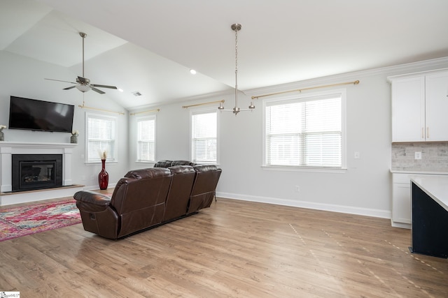 living room with ceiling fan with notable chandelier, vaulted ceiling, and light wood-type flooring