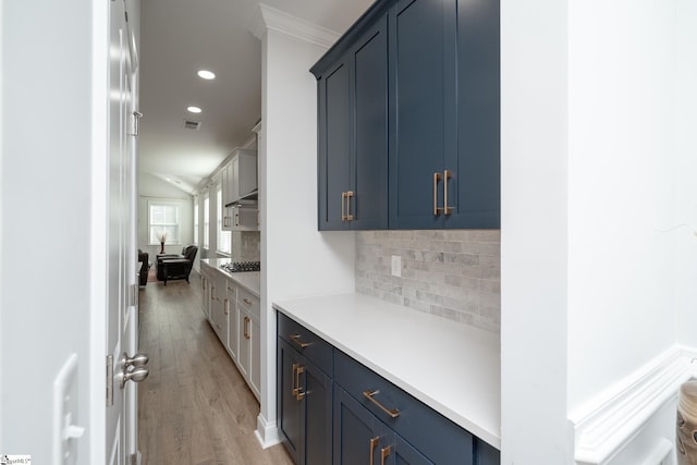 interior space featuring decorative backsplash, ornamental molding, blue cabinetry, light hardwood / wood-style floors, and stainless steel gas stovetop