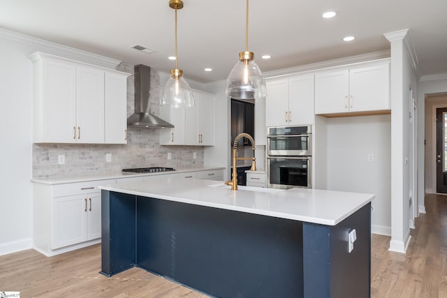 kitchen featuring white cabinetry, an island with sink, hanging light fixtures, and wall chimney range hood