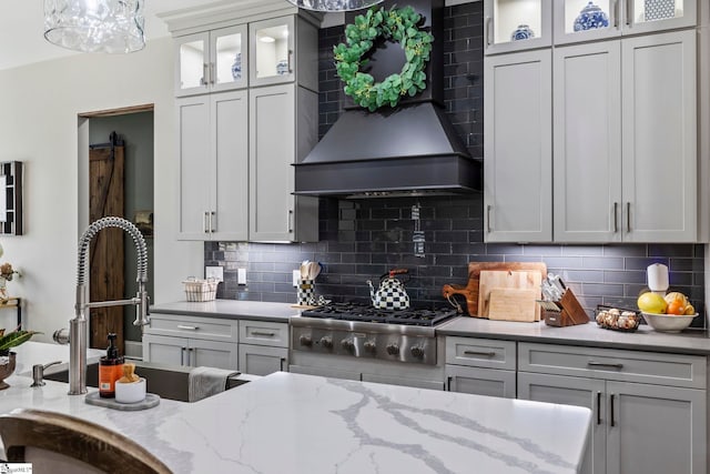 kitchen with decorative backsplash, light stone counters, custom range hood, and stainless steel gas cooktop