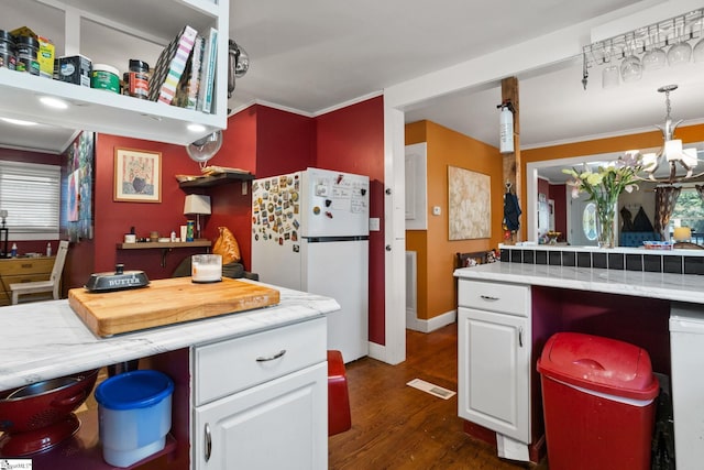 kitchen featuring dark wood-type flooring, white cabinets, white refrigerator, crown molding, and a chandelier