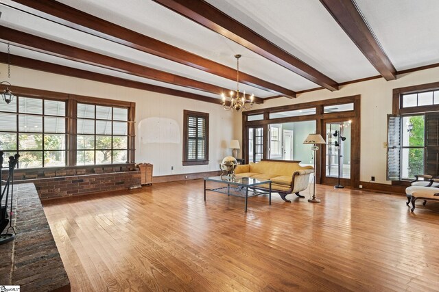 living room featuring beamed ceiling, plenty of natural light, light wood-type flooring, and a chandelier