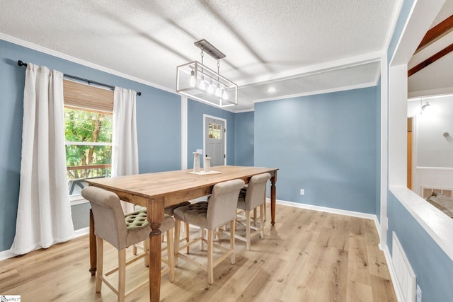 dining space featuring a textured ceiling, light wood-type flooring, and ornamental molding