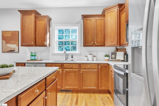 kitchen with decorative backsplash, stove, sink, refrigerator with ice dispenser, and light hardwood / wood-style floors