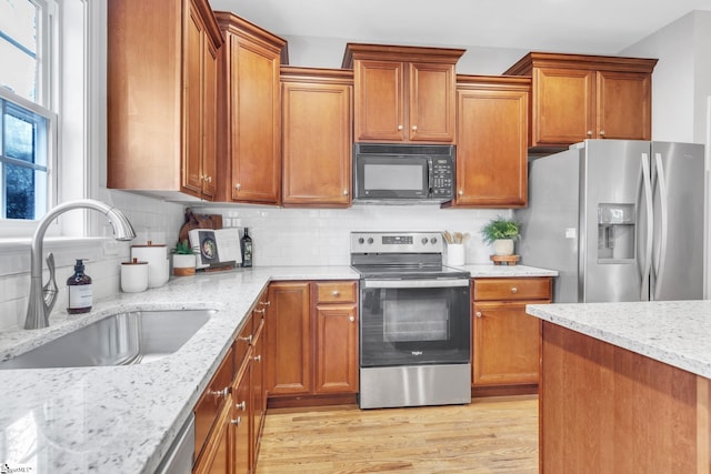 kitchen with light stone countertops, sink, tasteful backsplash, appliances with stainless steel finishes, and light wood-type flooring