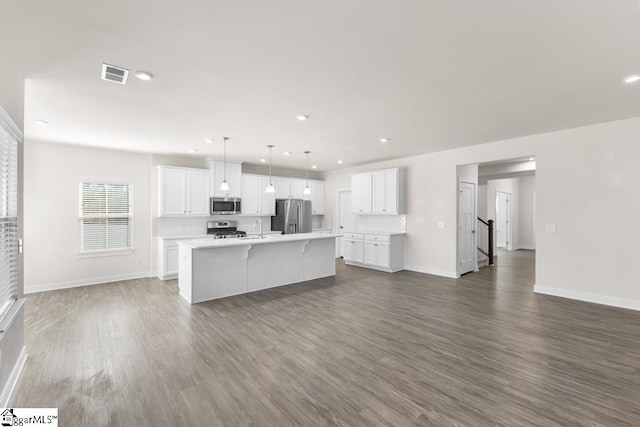 kitchen with appliances with stainless steel finishes, white cabinetry, dark wood-type flooring, and an island with sink