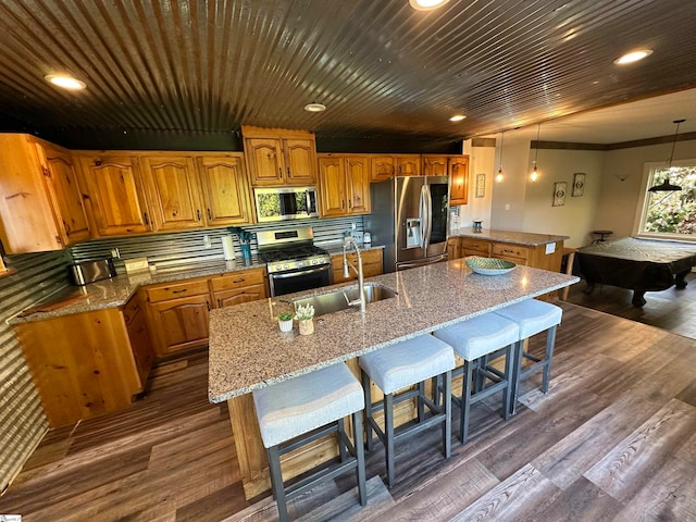 kitchen with pendant lighting, stainless steel appliances, dark hardwood / wood-style floors, and a center island with sink