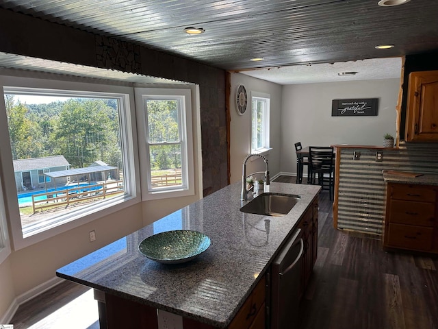 kitchen featuring sink, dark wood-type flooring, stainless steel dishwasher, dark stone countertops, and an island with sink