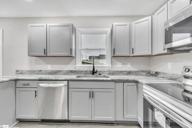 kitchen featuring appliances with stainless steel finishes, light stone counters, gray cabinetry, and sink