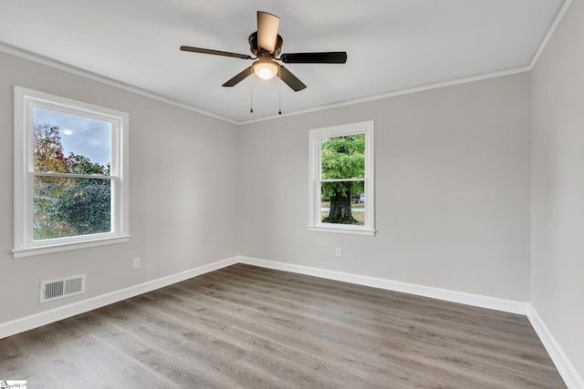 empty room with a wealth of natural light, hardwood / wood-style floors, ceiling fan, and ornamental molding