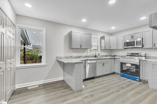 kitchen with light stone countertops, appliances with stainless steel finishes, sink, light hardwood / wood-style flooring, and gray cabinets