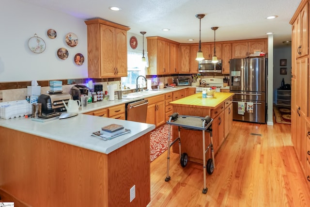 kitchen with a center island, hanging light fixtures, sink, light wood-type flooring, and appliances with stainless steel finishes