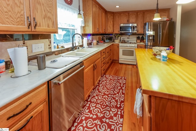 kitchen featuring sink, tasteful backsplash, pendant lighting, appliances with stainless steel finishes, and light wood-type flooring