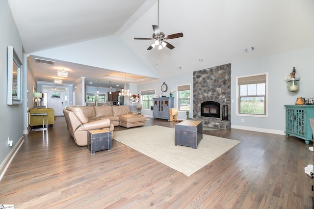 living room with hardwood / wood-style flooring, ceiling fan with notable chandelier, a stone fireplace, and high vaulted ceiling