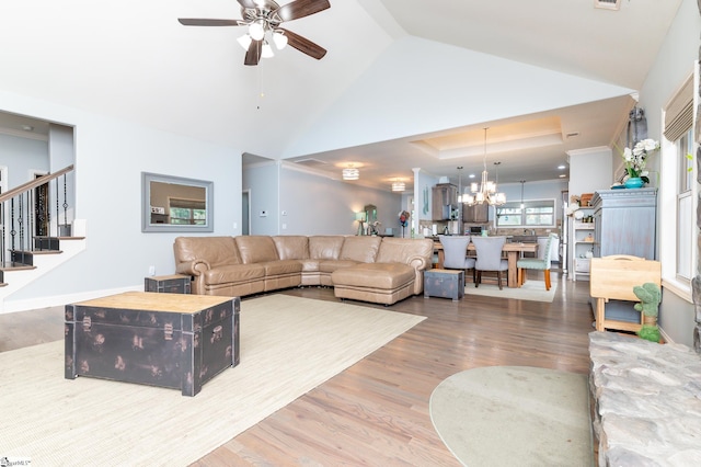 living room with ceiling fan with notable chandelier, hardwood / wood-style flooring, a raised ceiling, and lofted ceiling