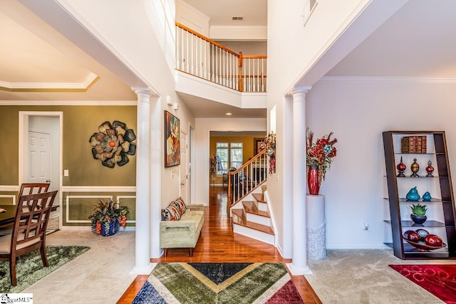 carpeted entryway with a towering ceiling, crown molding, and decorative columns