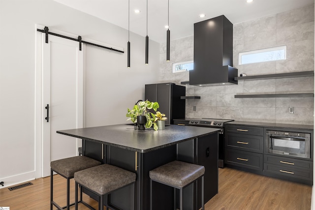 kitchen with stainless steel range with electric stovetop, a barn door, a breakfast bar area, and range hood