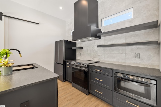 kitchen with sink, wall chimney exhaust hood, decorative backsplash, appliances with stainless steel finishes, and light wood-type flooring