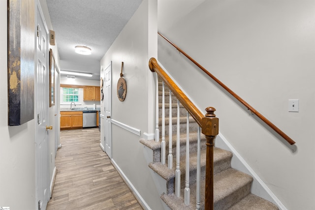 stairs with hardwood / wood-style floors, a textured ceiling, and sink