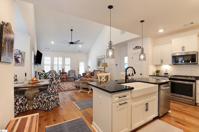 kitchen with white cabinets, a kitchen island with sink, appliances with stainless steel finishes, and light hardwood / wood-style flooring