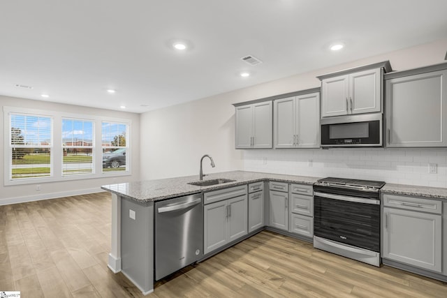 kitchen featuring sink, light stone countertops, light wood-type flooring, appliances with stainless steel finishes, and kitchen peninsula