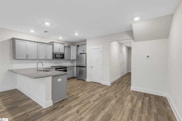 kitchen featuring kitchen peninsula, light stone countertops, stainless steel appliances, sink, and gray cabinets