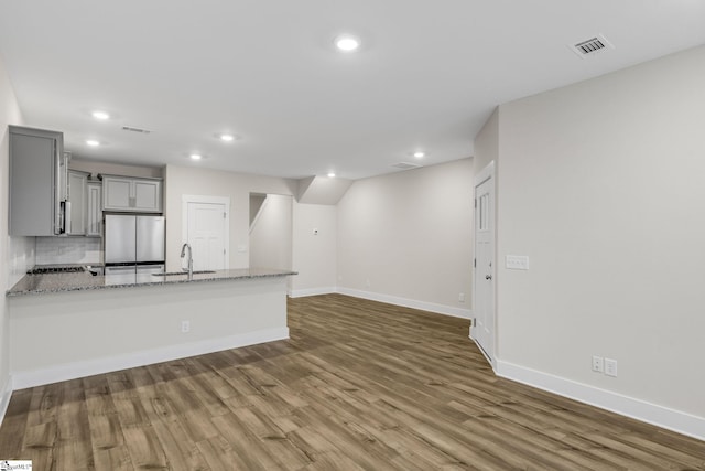 interior space featuring hardwood / wood-style flooring, decorative backsplash, gray cabinets, stainless steel fridge, and light stone countertops