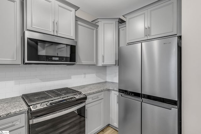 kitchen featuring decorative backsplash, light stone countertops, stainless steel appliances, and light wood-type flooring