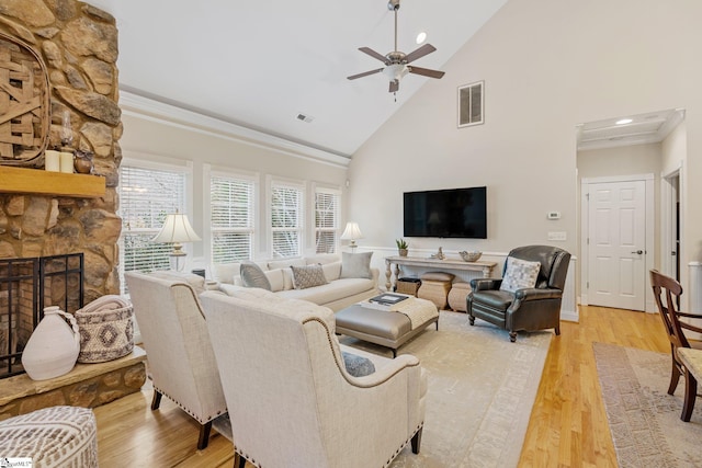 living room featuring light wood-type flooring, ceiling fan, crown molding, high vaulted ceiling, and a fireplace