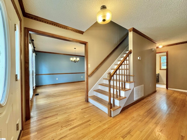 stairway featuring crown molding, hardwood / wood-style floors, a textured ceiling, and an inviting chandelier