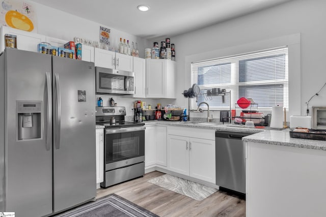 kitchen featuring white cabinets, sink, light stone countertops, light wood-type flooring, and stainless steel appliances