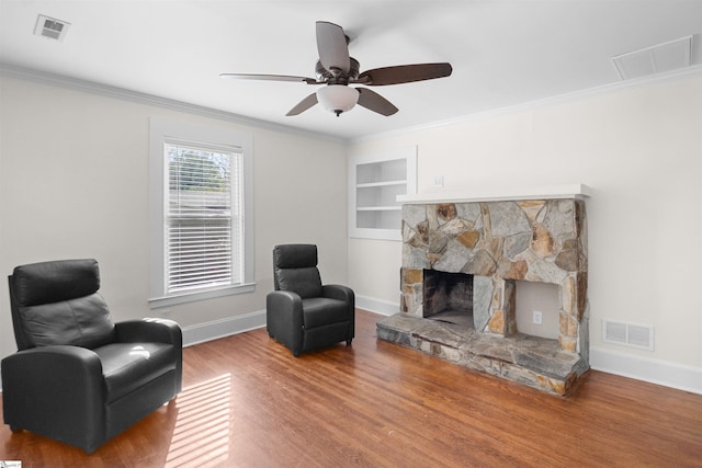 living area with hardwood / wood-style flooring, ceiling fan, a stone fireplace, and ornamental molding