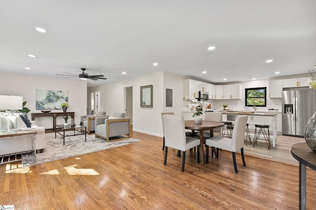 dining space with electric panel, light hardwood / wood-style floors, ceiling fan, and sink