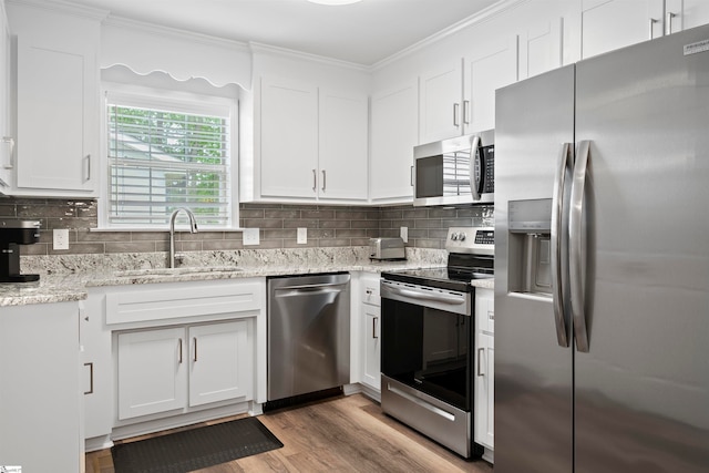 kitchen with sink, stainless steel appliances, light stone counters, white cabinets, and light wood-type flooring