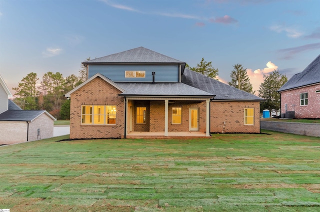 back house at dusk with a patio, central AC, and a lawn