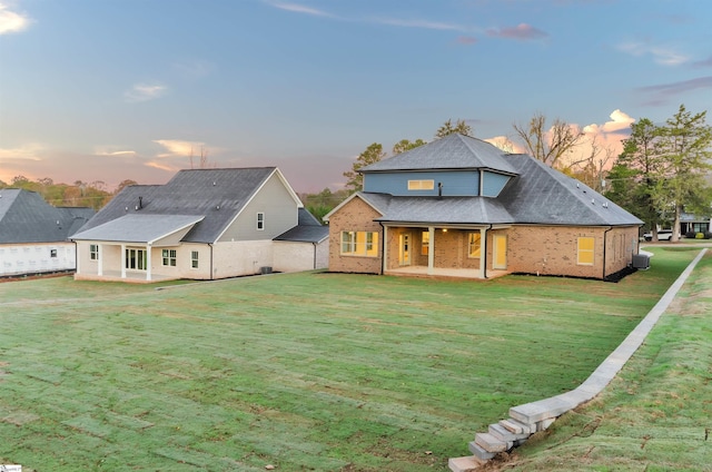 back house at dusk featuring a lawn