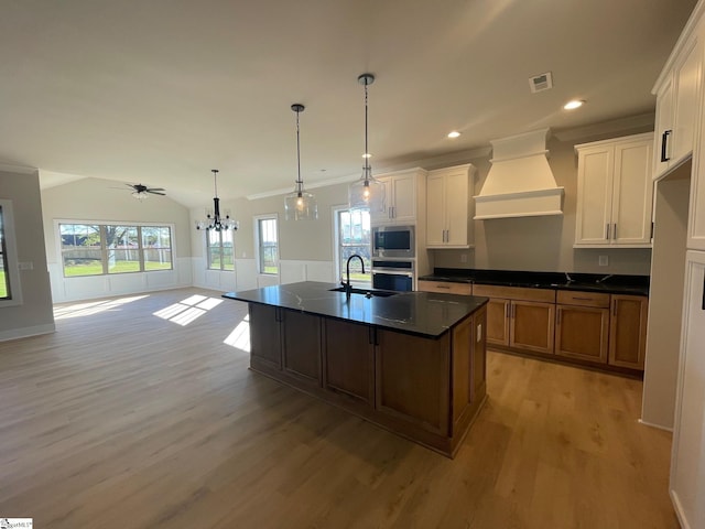 kitchen with appliances with stainless steel finishes, hanging light fixtures, white cabinets, a center island with sink, and custom exhaust hood